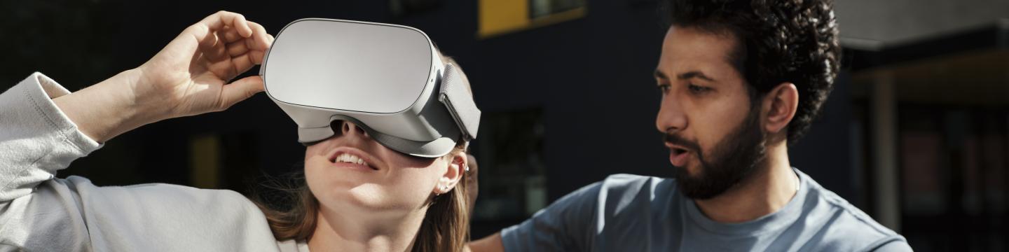A woman wearing virtual reality headset and a man is helping her. 