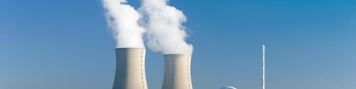 Nuclear power plant with two steaming cooling towers in a blue sky.