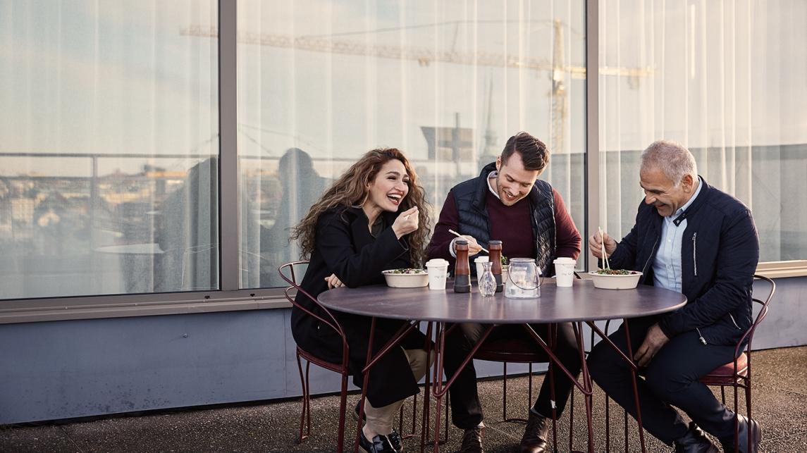 A woman and two men eating lunch outside. 