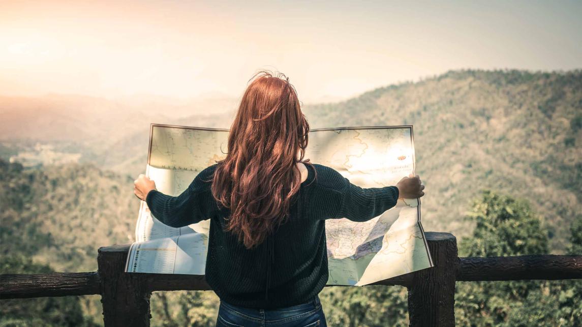 Young woman holding a large map in front of a vast forest area,