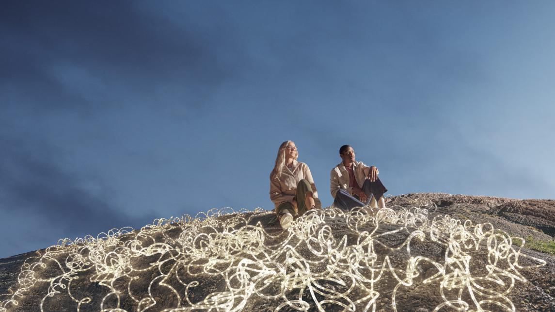 Expansive dark blue-sky backdrop, with a man and woman in the foreground surrounded by white LED rope lights.