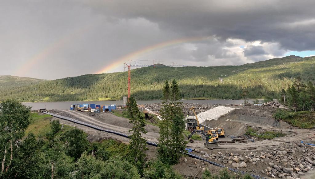 A rainbow over a lake and dam construction site in Swedish hills.