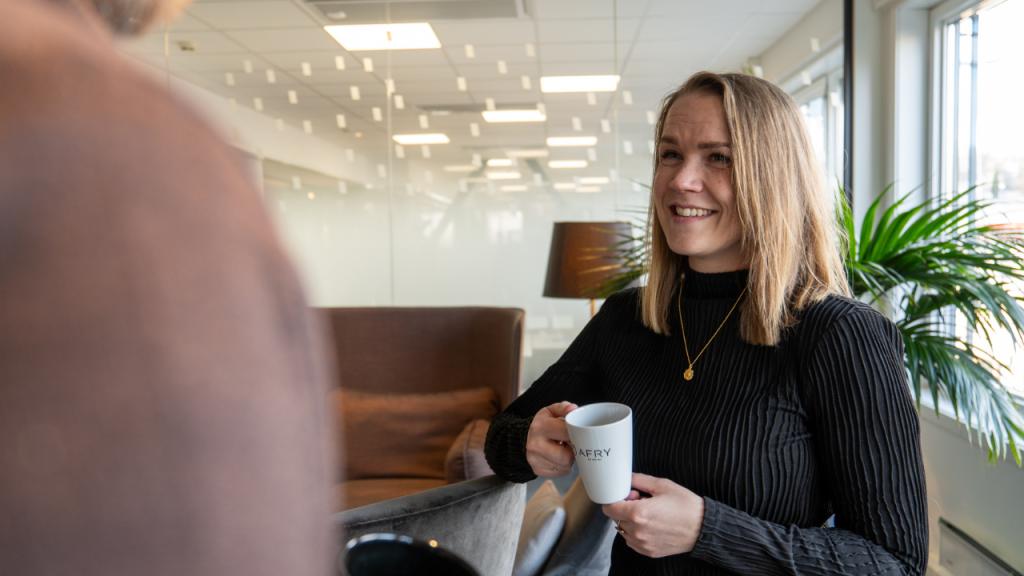 Kvinne med kaffekopp som smiler i en samtale