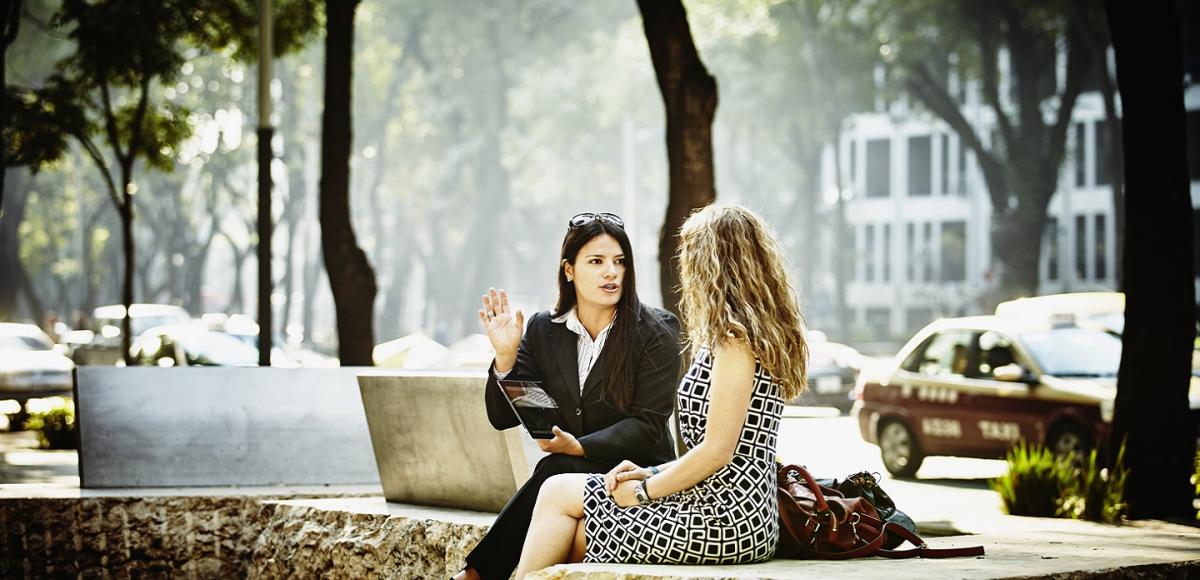 Two women sitting on a bench, talking. 