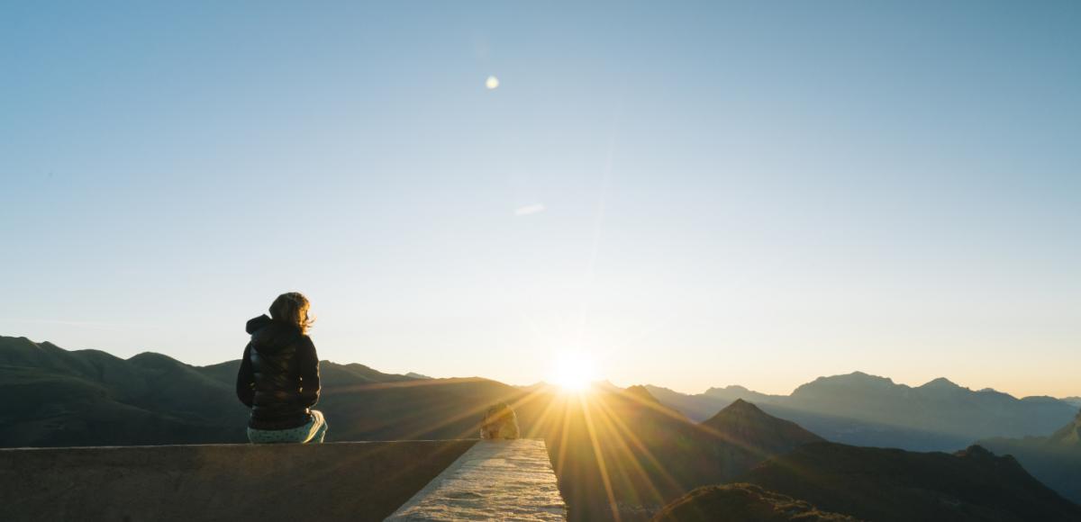 Person looking out over sunrise above mountain peaks