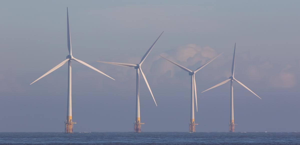 Offshore wind turbines. Green energy. Row of four environmentally friendly wind powered turbines on the sea horizon off the coast of Great Yarmouth UK.