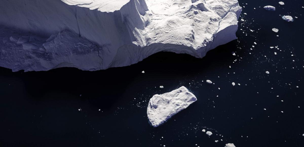 Ice block breaking off iceberg into deep blue ocean