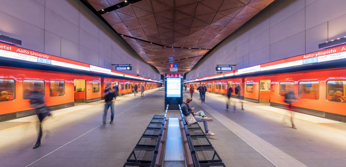 Bild på tågstation med folk och två tåg som åker i hög hastighet