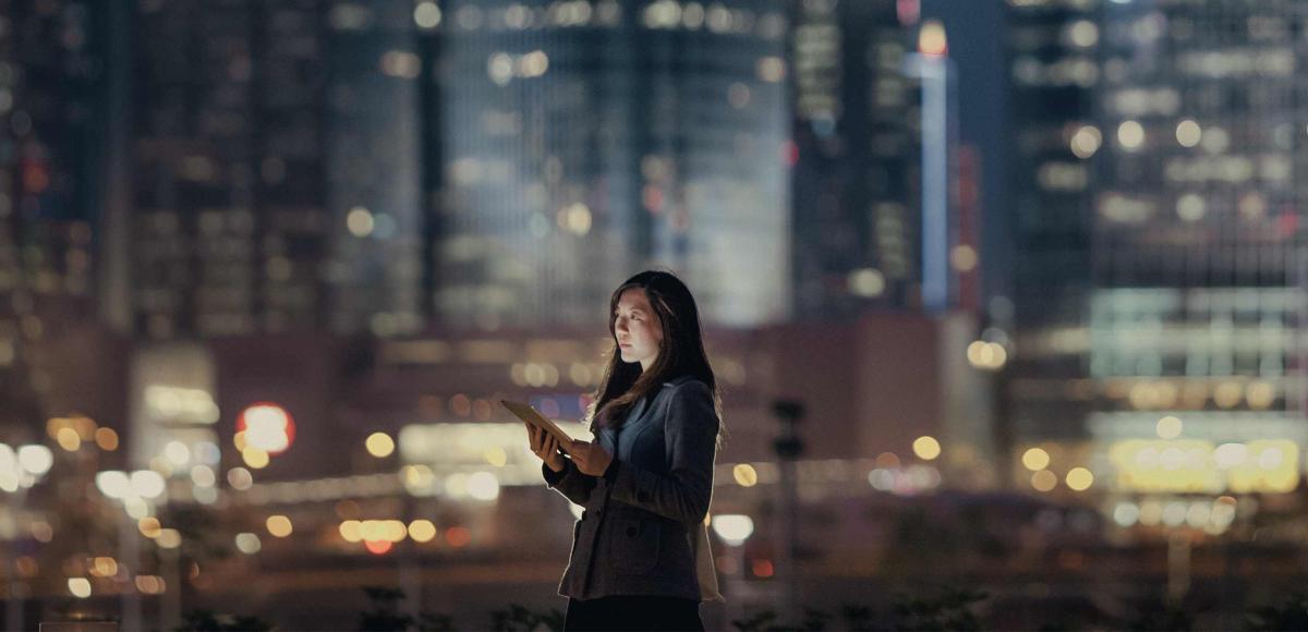 Woman holding tablet walking in nighttime urban environment