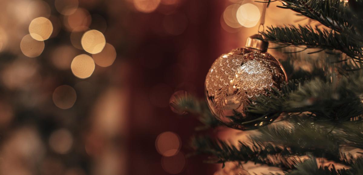 Gold bauble hanging from a fir tree with fairy lights in background