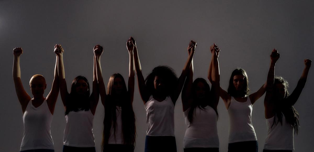 Several women holding hands with arms up high, a powerful line of women