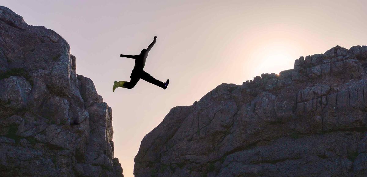 Person jumping over gap between two cliffs