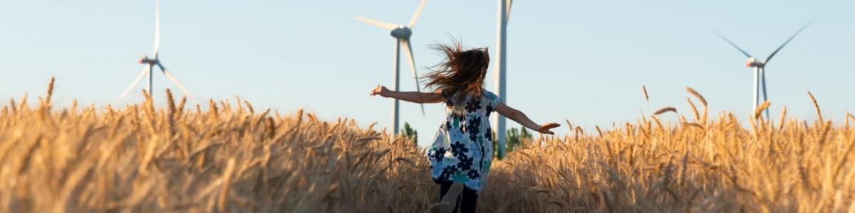 Girl in floral dress running through field towards wind turbines