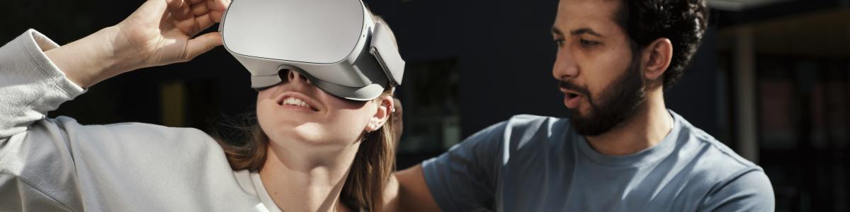 A woman wearing virtual reality headset and a man is helping her. 