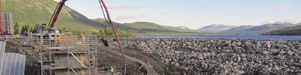 Construction site of a rock fill dam below a lake.