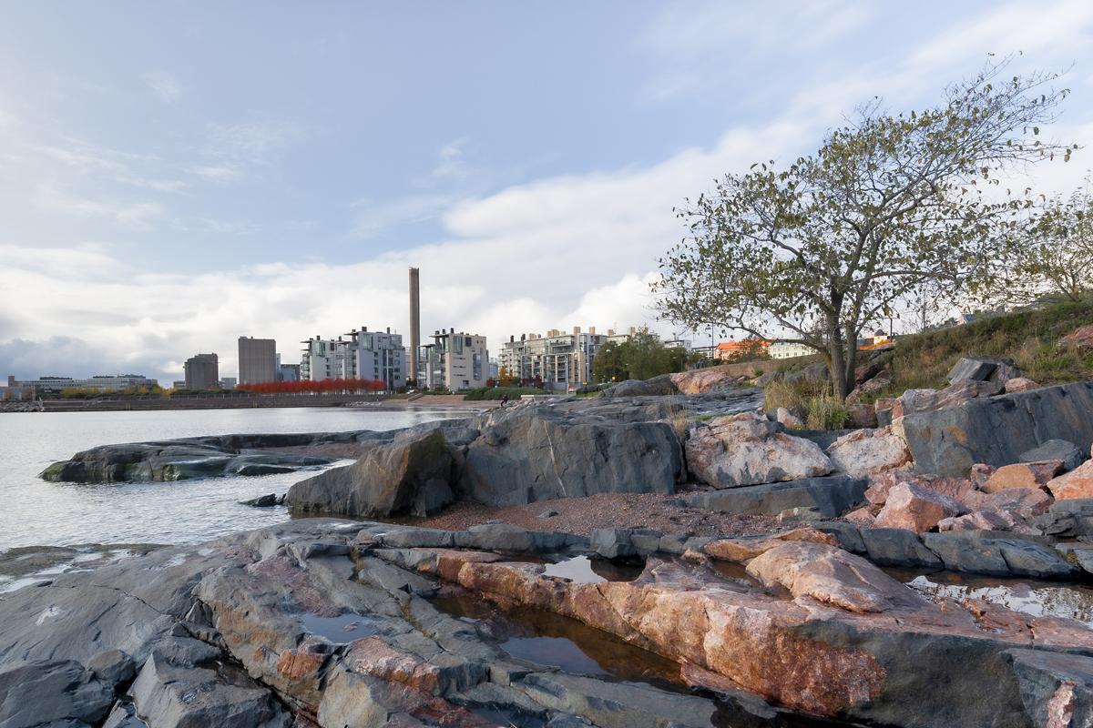 View by the water, rocks in the shore, buildings in the background