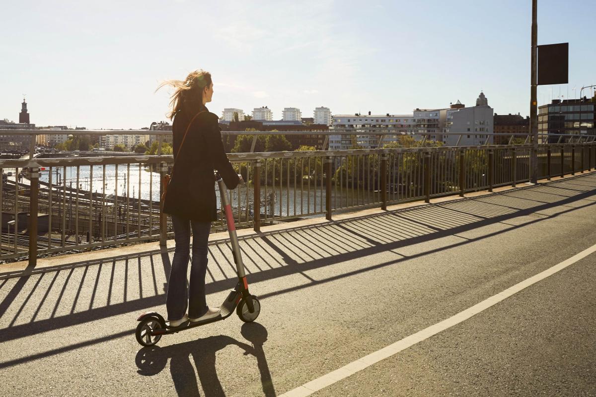 A woman rides a scooter across a bridge