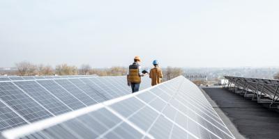 View on the rooftop solar power plant with two engineers walking and examining photovoltaic panels. Concept of alternative energy and its service