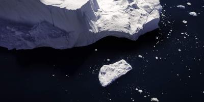 Ice block breaking off iceberg into deep blue ocean
