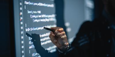 A man pointing at a wall with code projected onto it