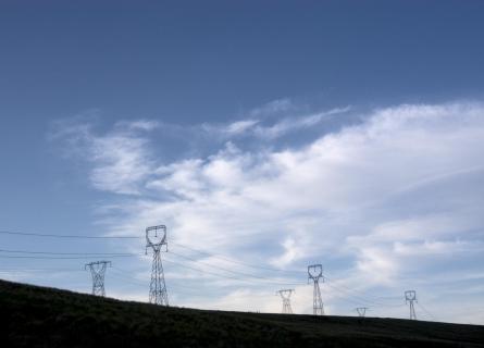 Powerlines on hill against blue sky