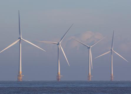 Offshore wind turbines. Green energy. Row of four environmentally friendly wind powered turbines on the sea horizon off the coast of Great Yarmouth UK.