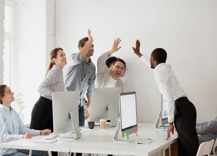 People around working table raise hands in happiness