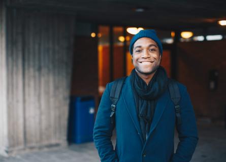 Portrait of smiling man wearing blue warm clothing and knit hat standing in campus