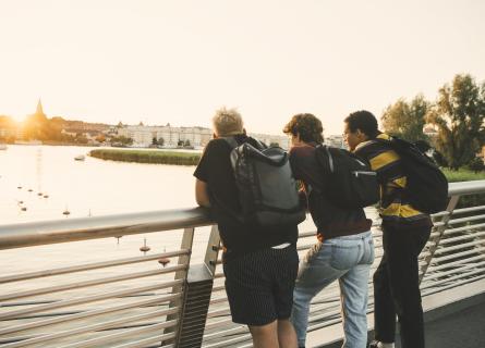 Rear view of young man with teenage friends standing against railing in city