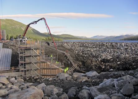 Construction site of a rock fill dam below a lake.
