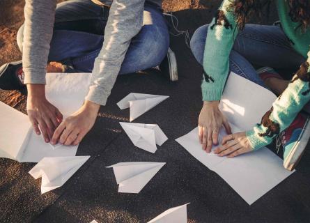 Two persons folding paper planes, using blank papers creatively