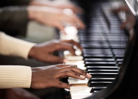 Two sets of hands playing the piano in cooperation