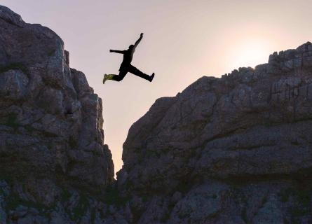 Person jumping over gap between two cliffs