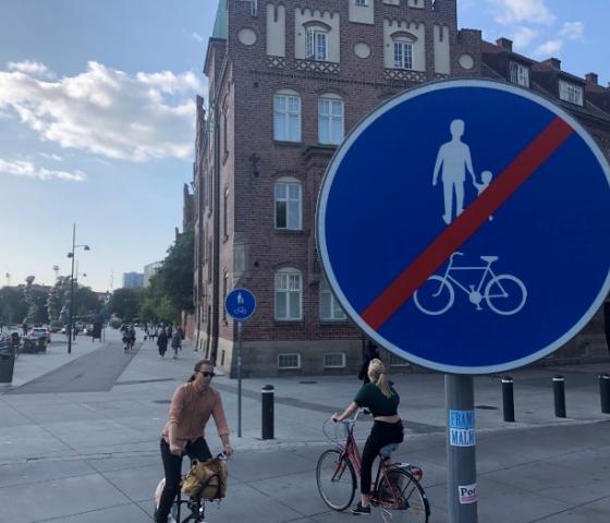 A sign showing that walking and biking is forbidden, and two women riding bikes in the background.