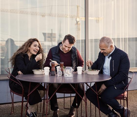 A woman and two men eating lunch outside. 