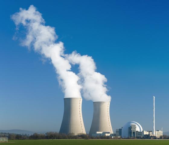 Nuclear power station with two steaming cooling towers in blue sky.