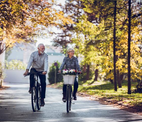 Senior couple bycycling throw forest in autumn