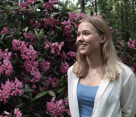 Siiri Kalliovalkama standing outdoors next to a pink Rhododendron.