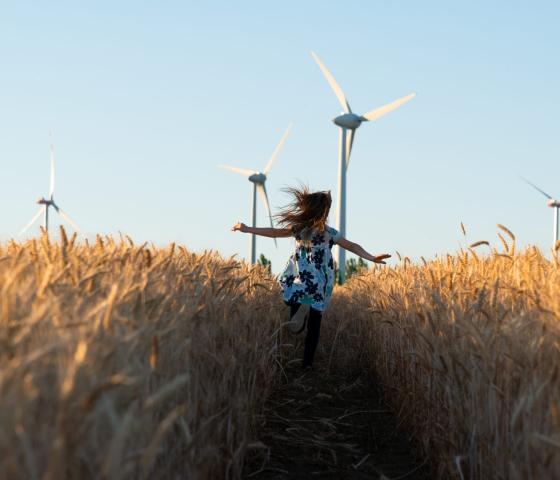 girl running trough a field with wind turbines